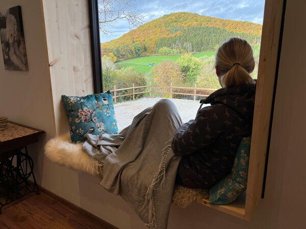 Eine Frau sitzt im gemütlichen Sitzfenster aus Zirbenholz im Landchalet Eifel auf dem Landgut Pfauenhof